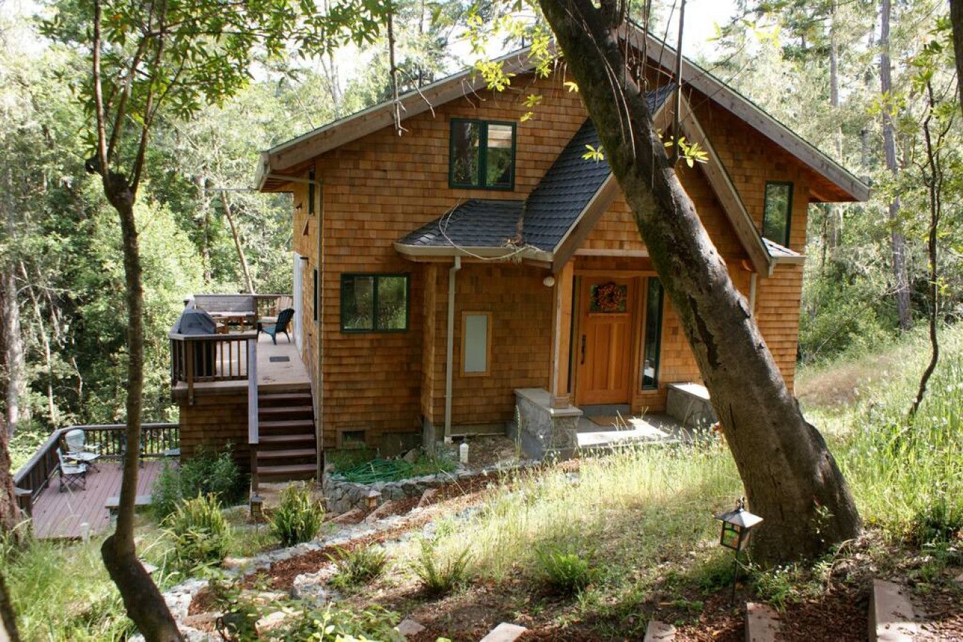 A wooden cabin with a deck, surrounded by trees.