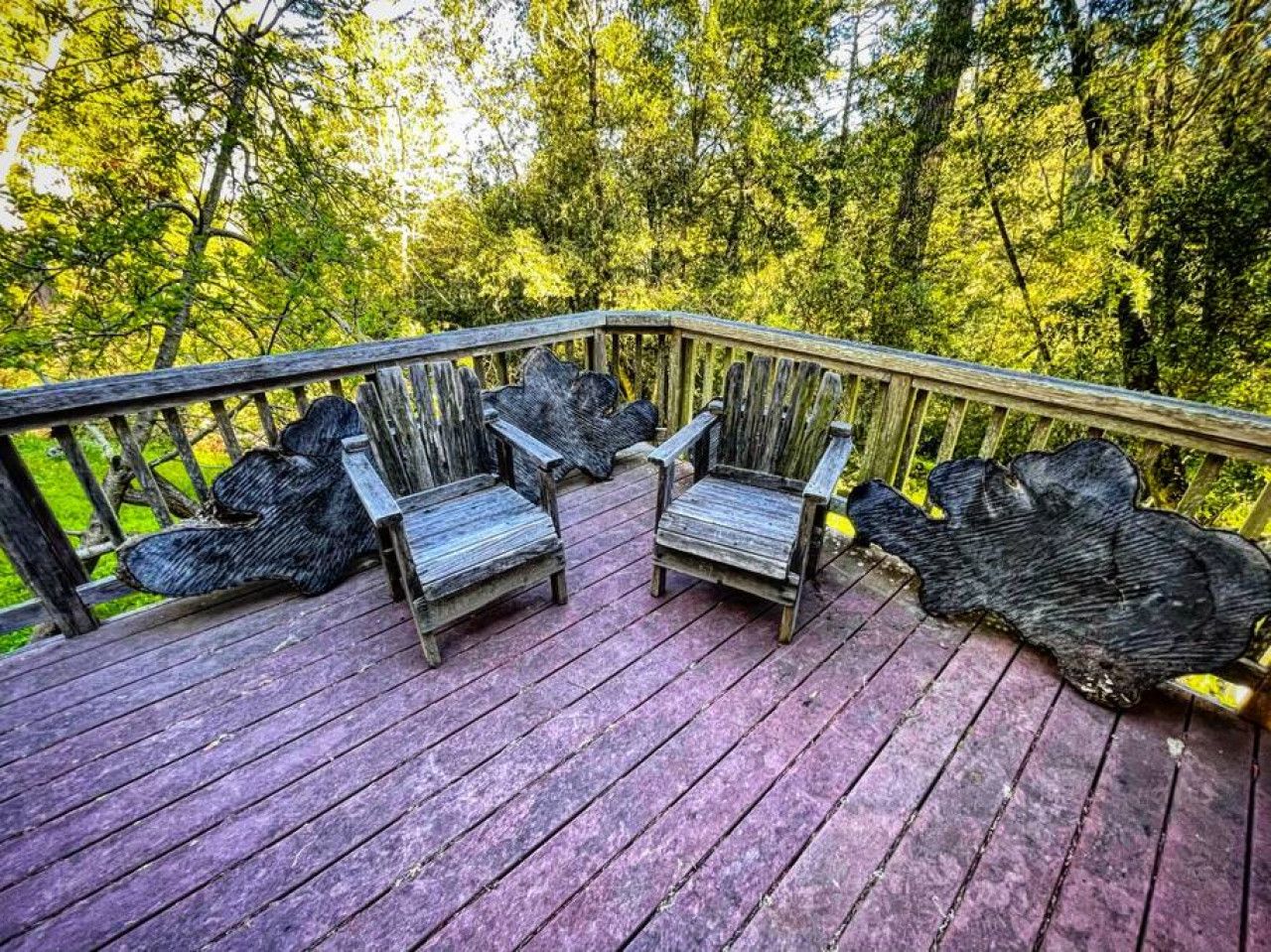 A wooden deck with two Adirondack chairs and a large tree stump.