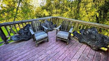 A wooden deck with two Adirondack chairs and a large tree stump.
