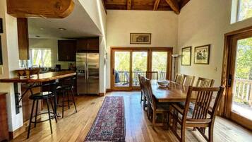 A spacious kitchen with wooden floors, a dining area with a large table and chairs, and a view through glass doors to an outdoor deck.