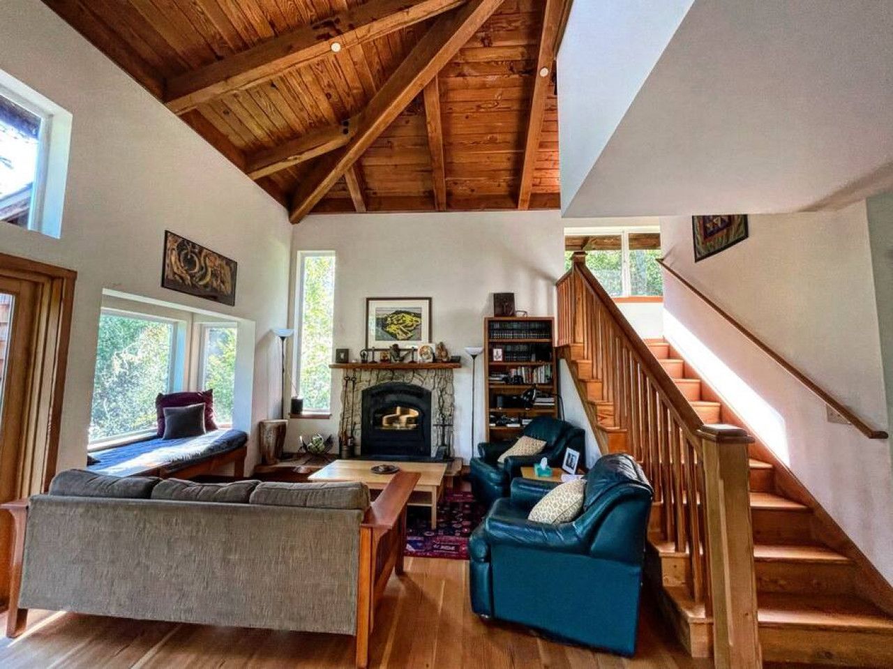 A cozy living room with a fireplace, wooden beams, and a staircase.