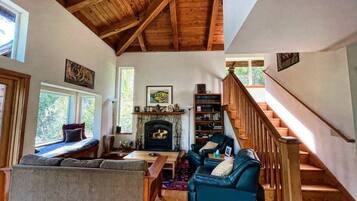 A cozy living room with a fireplace, wooden beams, and a staircase.