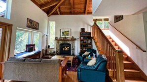A cozy living room with a fireplace, wooden beams, and a staircase. - Forest Getaway Cozy, Inviting Cabin w Deck (Inverness)