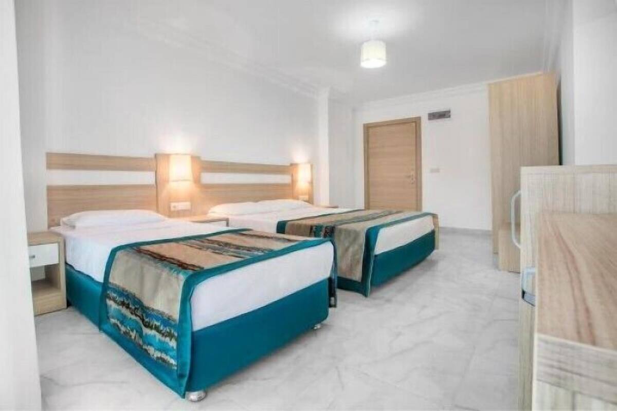 Ein Hotelzimmer mit zwei Einzelbetten, einem Holzschrank, einem Nachttisch und einem kleinen Schreibtisch.
