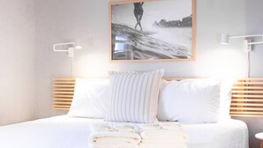 Ein ordentlich bezogenes Bett mit weißen Leinen und gestreiften Kissen, ein gerahmtes Foto darüber sowie zwei Nachttischlampen.