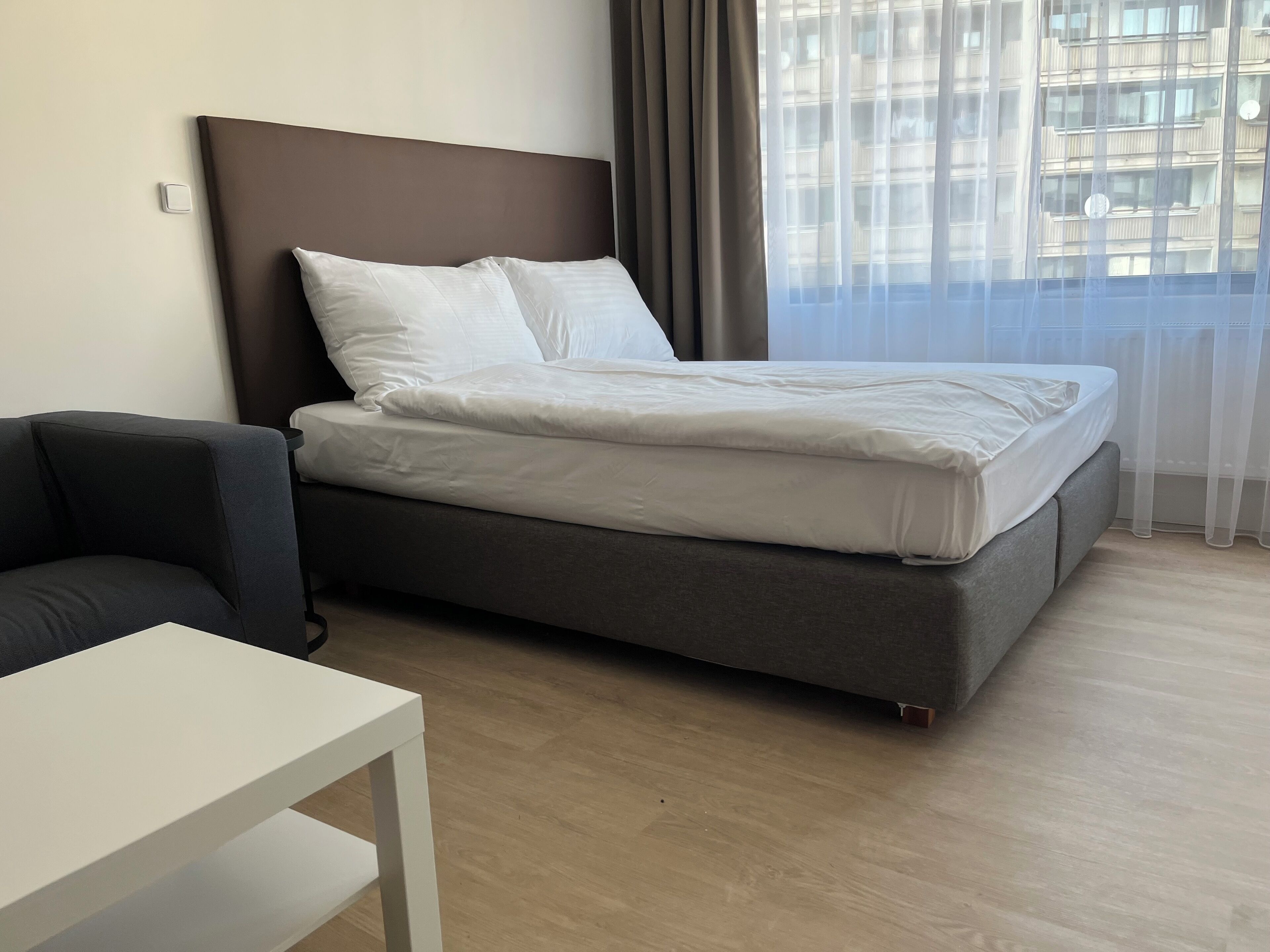 Una habitación de hotel moderna con una cama, una mesita y un ventanal con cortinas.
