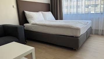 Una habitación de hotel moderna con una cama, una mesita y un ventanal con cortinas.