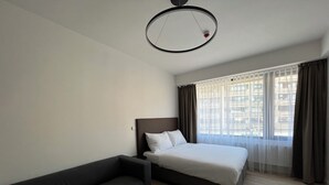A hotel room with a bed, a sofa, a small table, and a window with curtains. - Post 120 Suites (Prague)
