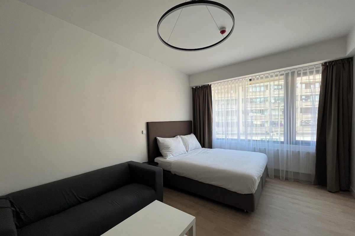 A hotel room with a bed, a sofa, a small table, and a window with curtains.
