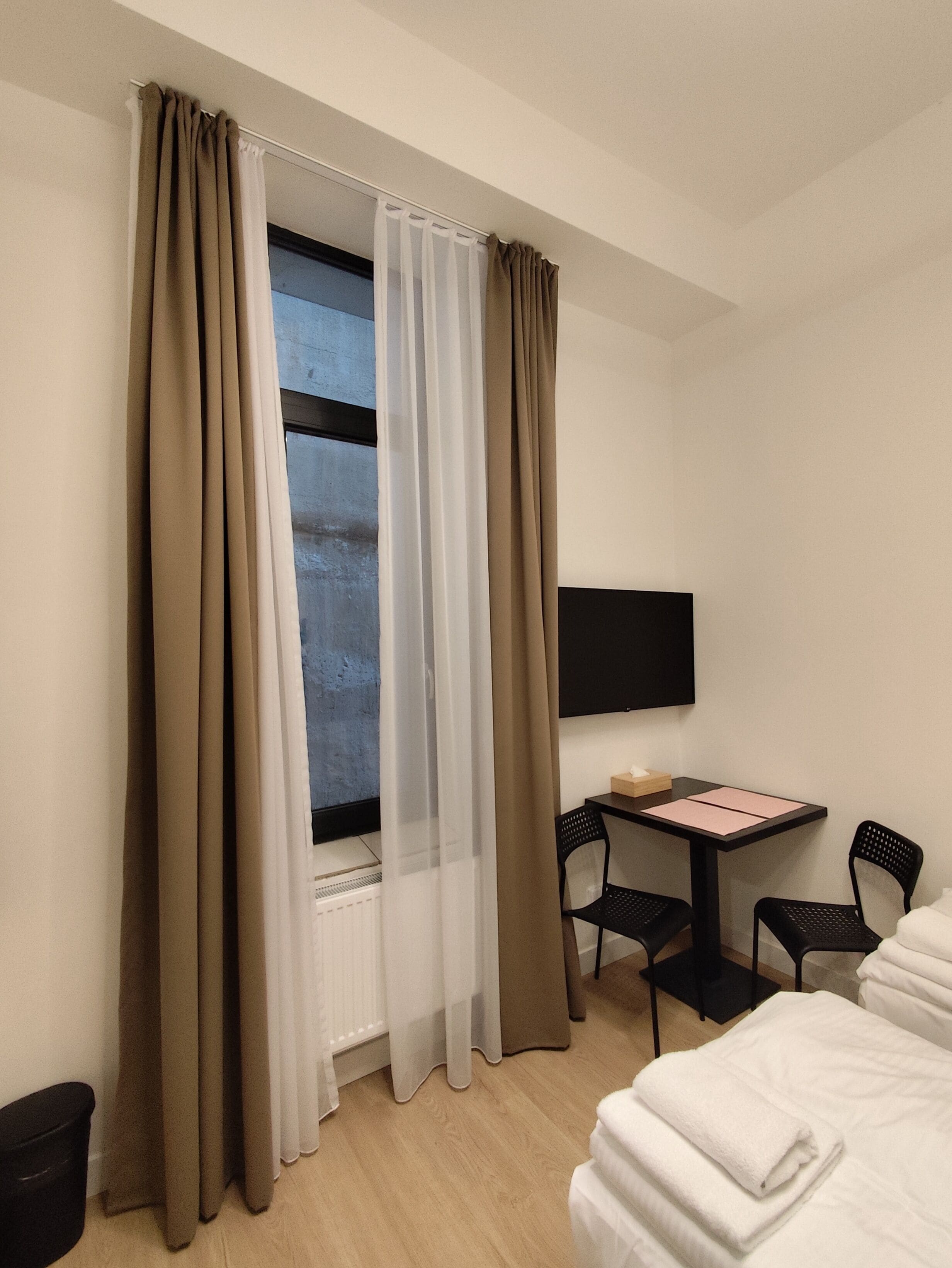 Une chambre d’hôtel avec un lit, un bureau et une chaise, un téléviseur fixé au mur et une fenêtre avec des rideaux.