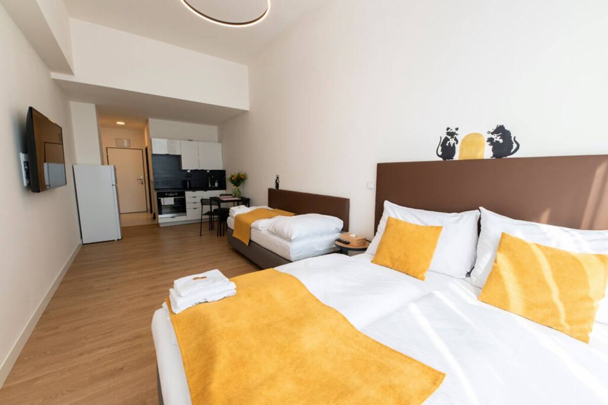 A hotel room with two beds, a kitchenette, and a TV.