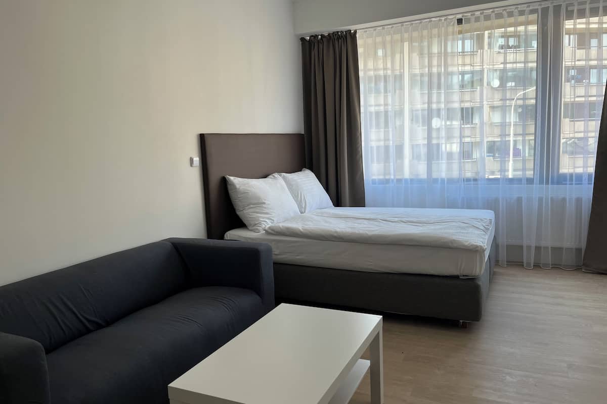 A modern hotel room with a bed, a dark-colored sofa, and a white table.