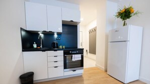 A modern kitchen with white cabinets, a black countertop, a built-in oven, and a white refrigerator. - Post 120 Suites (Prague)