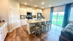 Una cocina moderna con armarios blancos, una isla central con taburetes y un amplio ventanal con vistas al exterior.