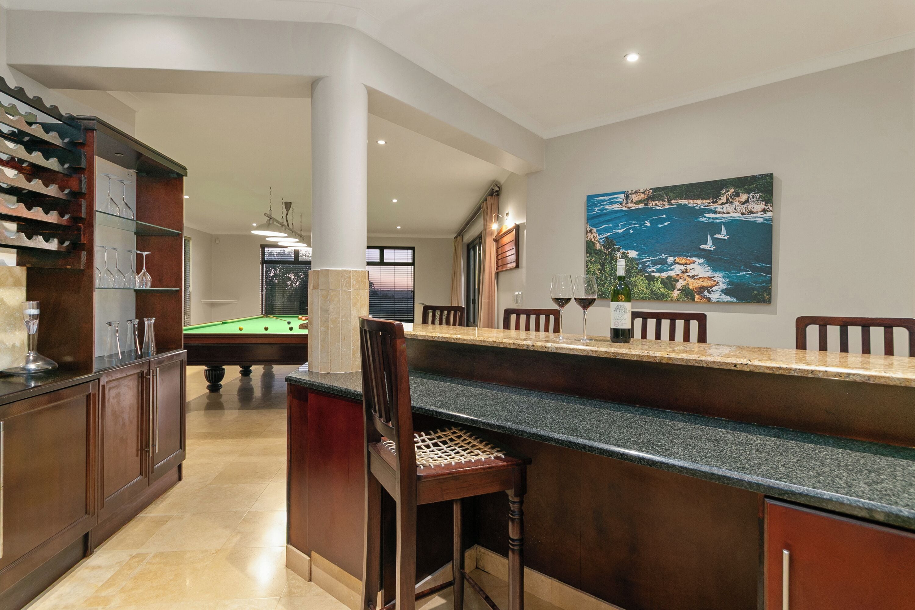 Un espace bar équipé d’une table de billard, de tabourets et d’un tableau représentant un paysage côtier.