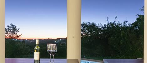 An outdoor patio with a pool, a table with a bottle and glasses, and chairs.