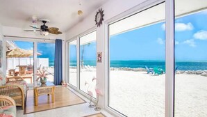 A beachside room with large windows, a ceiling fan, wicker furniture, and a view of the beach and ocean.