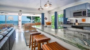 A modern kitchen with a large island, built-in appliances, and a view to the sea.