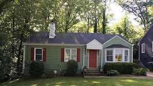 A green house with a red door and white trim, surrounded by trees and a well-maintained lawn.