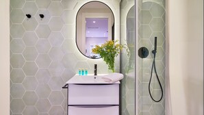 A bathroom with a hexagonal tile wall, a white sink with a mirror, a towel, and a shower with a glass door.