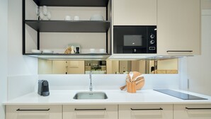 A modern kitchen with a white countertop, stainless steel sink, and black appliances. There are shelves above the counter holding dishes and glasses.
