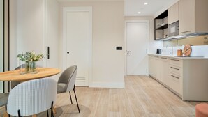 A modern kitchen with light wood cabinets, a wooden dining table, and a grey upholstered chair.