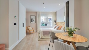 A modern hotel room with a large bed, a dining table, and a view of the city.