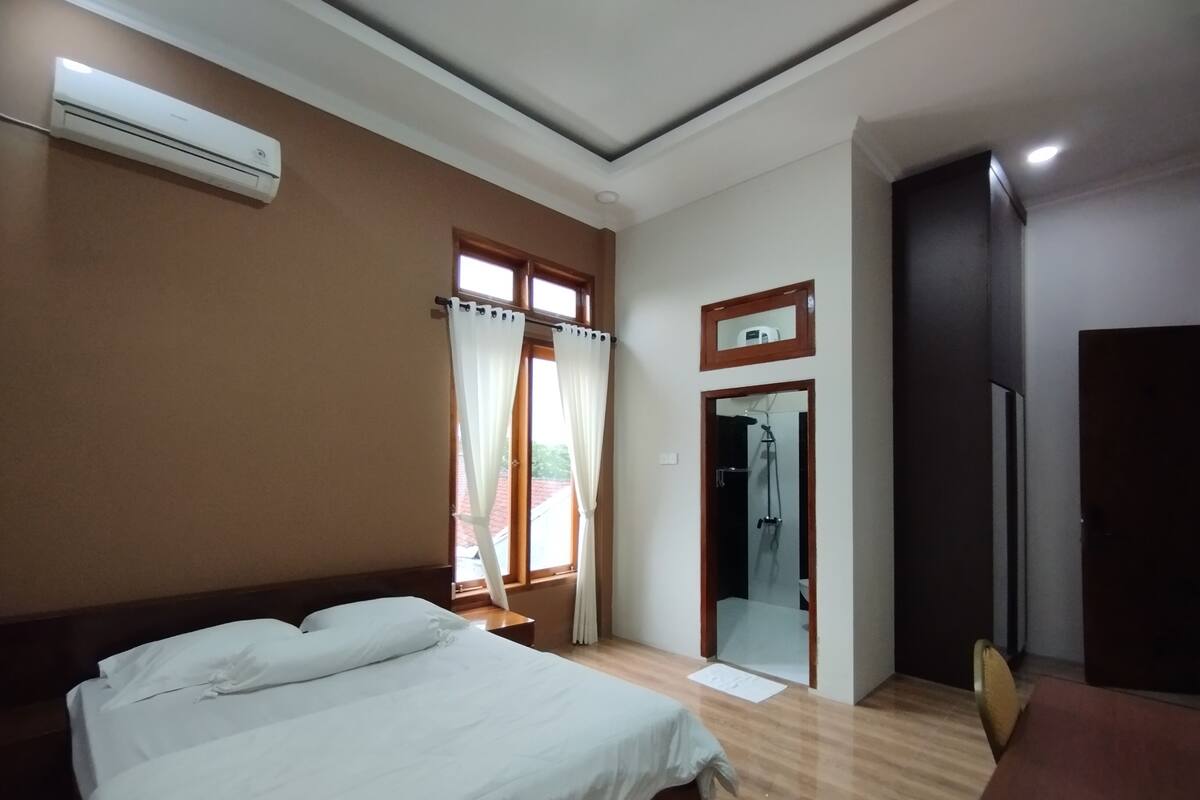 Een hotelkamer met een bed, een bureau, airconditioning, een douche en een deur.