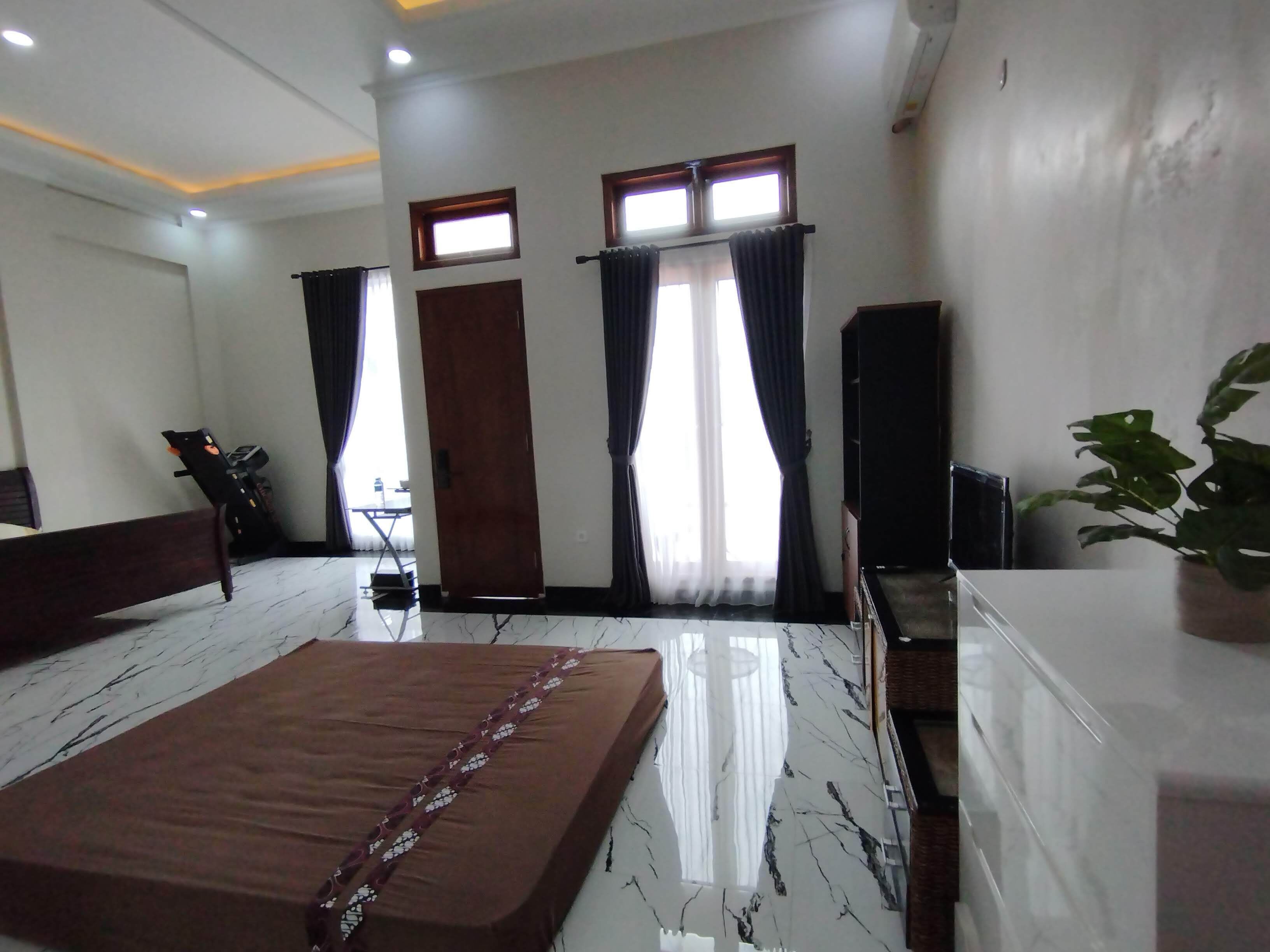 A bedroom with a bed, a desk, a chair, a radiator, and a potted plant.
