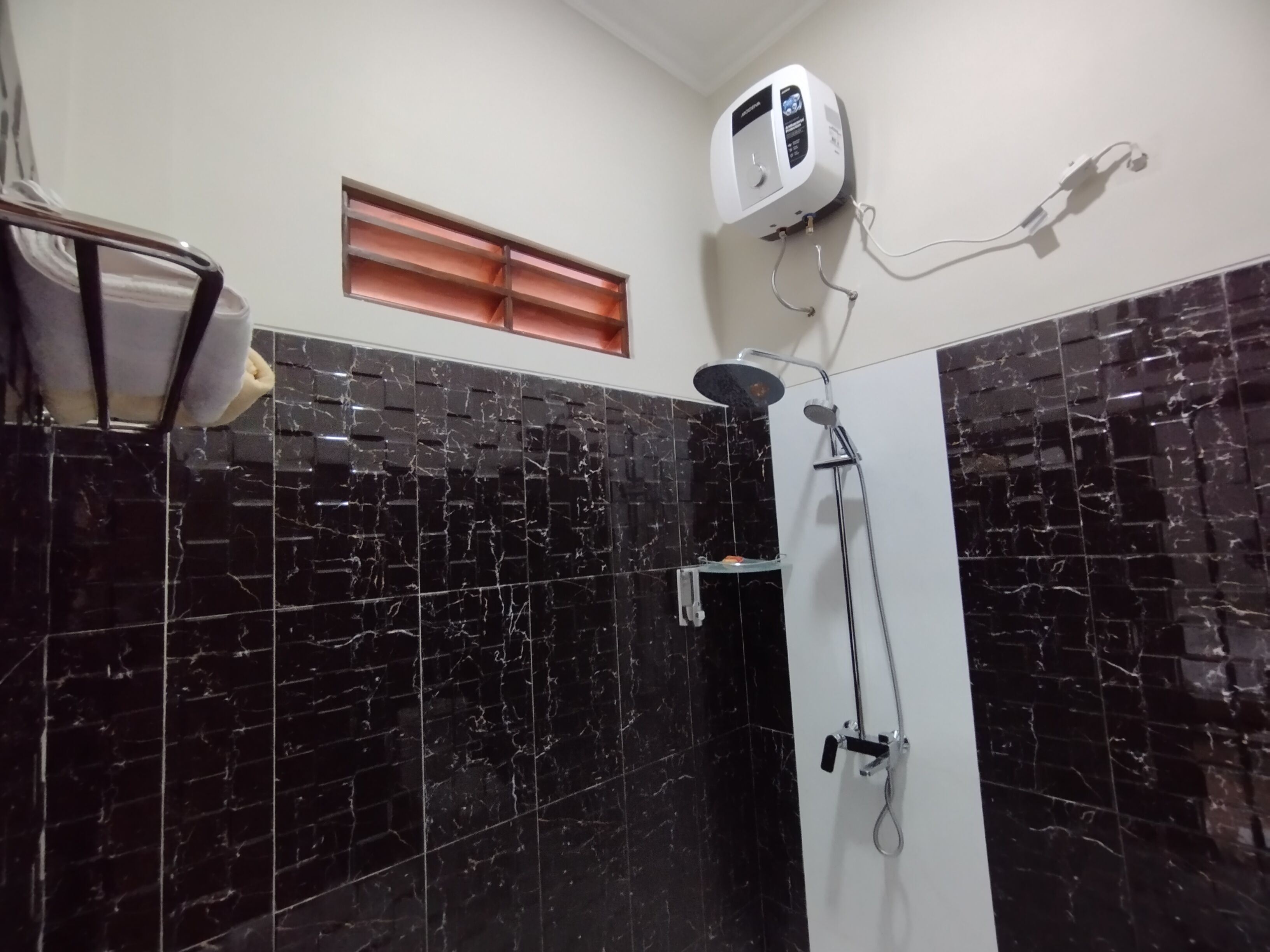 Une salle de bain avec des carreaux de marbre noir, une douche, un porte-serviettes et une petite fenêtre.