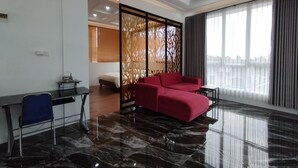 Une chambre d’hôtel moderne avec un canapé rouge, un bureau avec une chaise, un paravent décoratif et une grande fenêtre donnant sur un beau paysage.