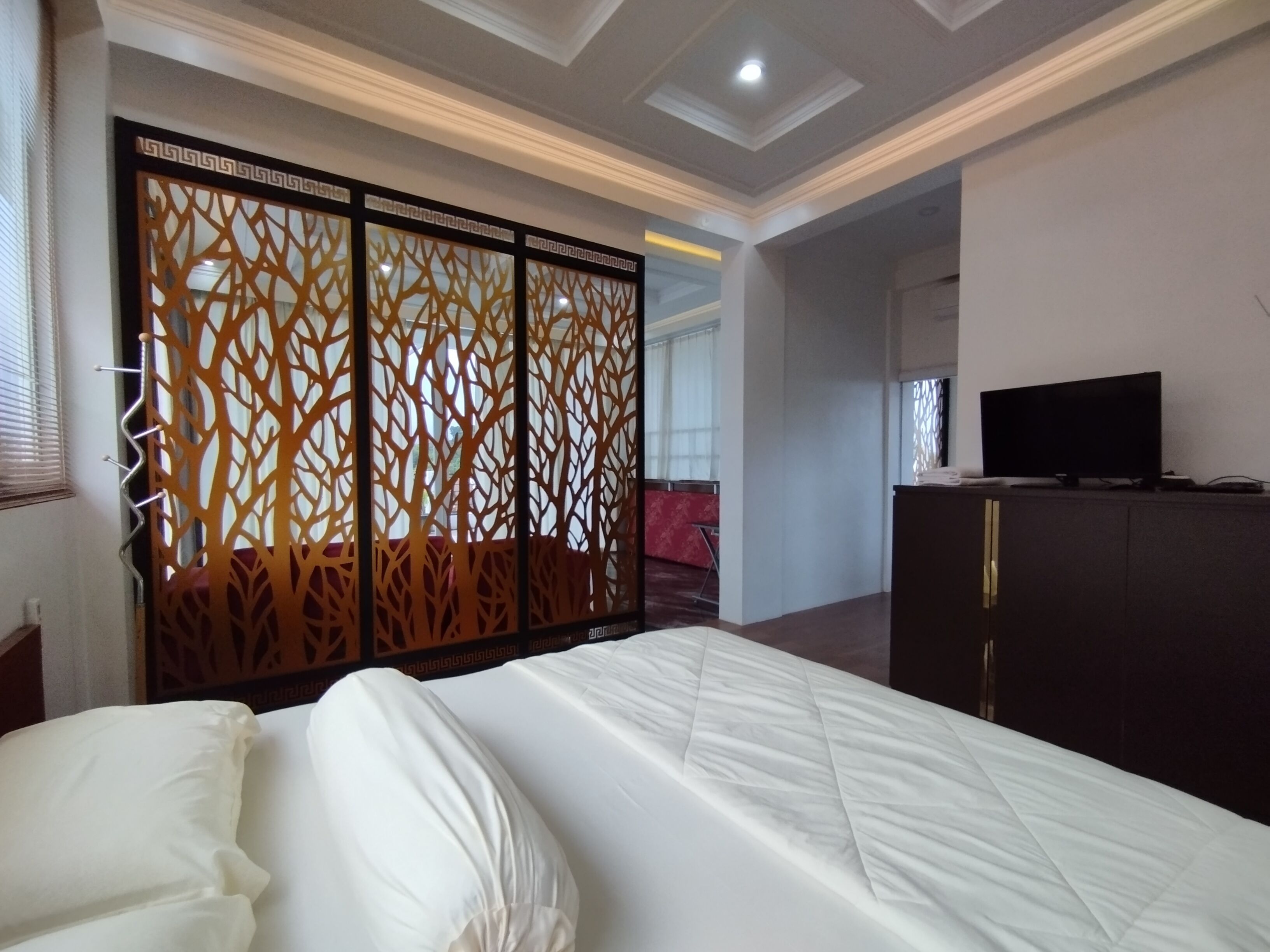 Quarto de hotel com uma cama, uma televisão sobre um móvel e um ecrã decorativo.