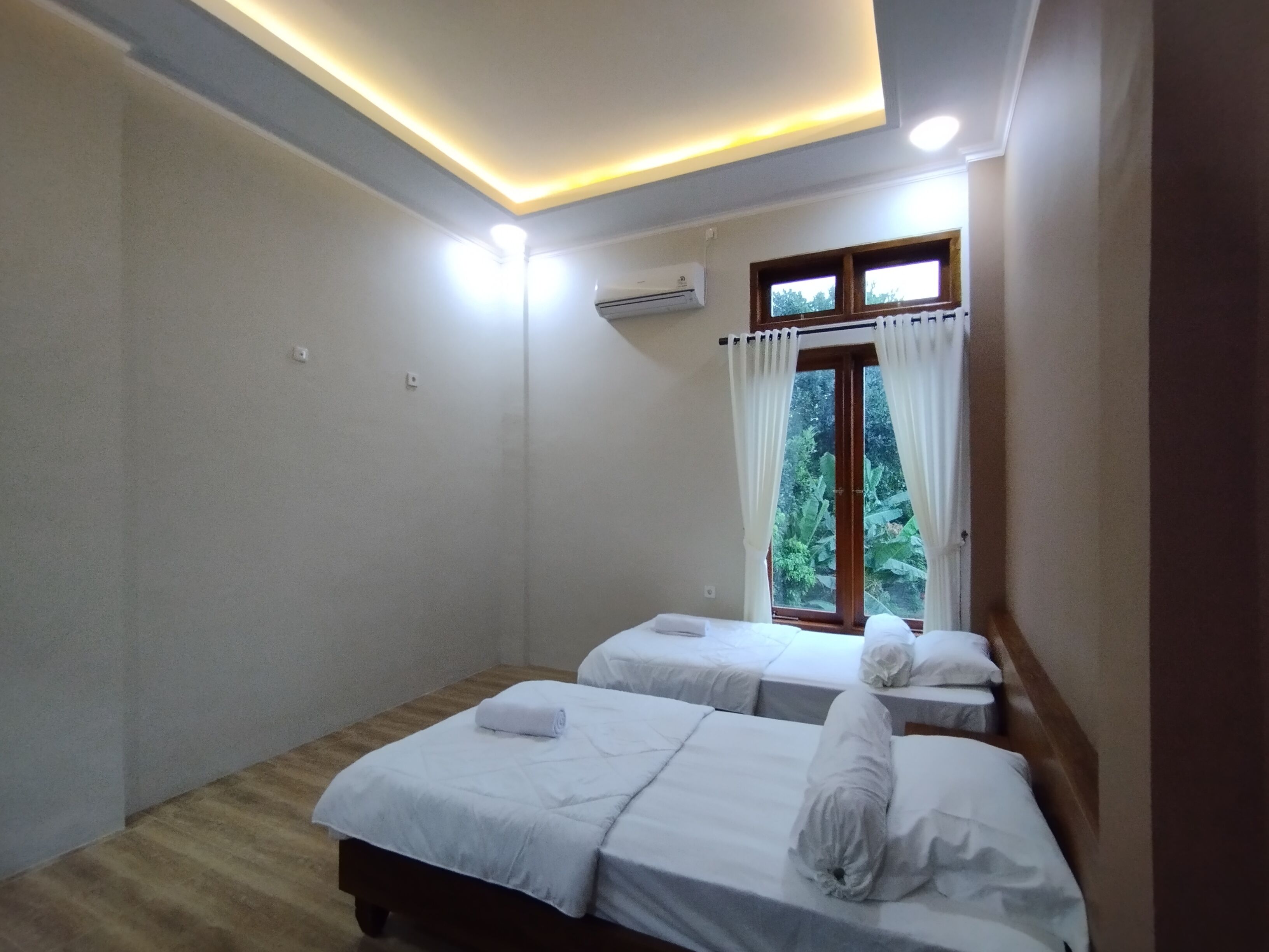 Een hotelkamer met twee bedden, een plafondlamp, een airconditioning en een raam met gordijnen.