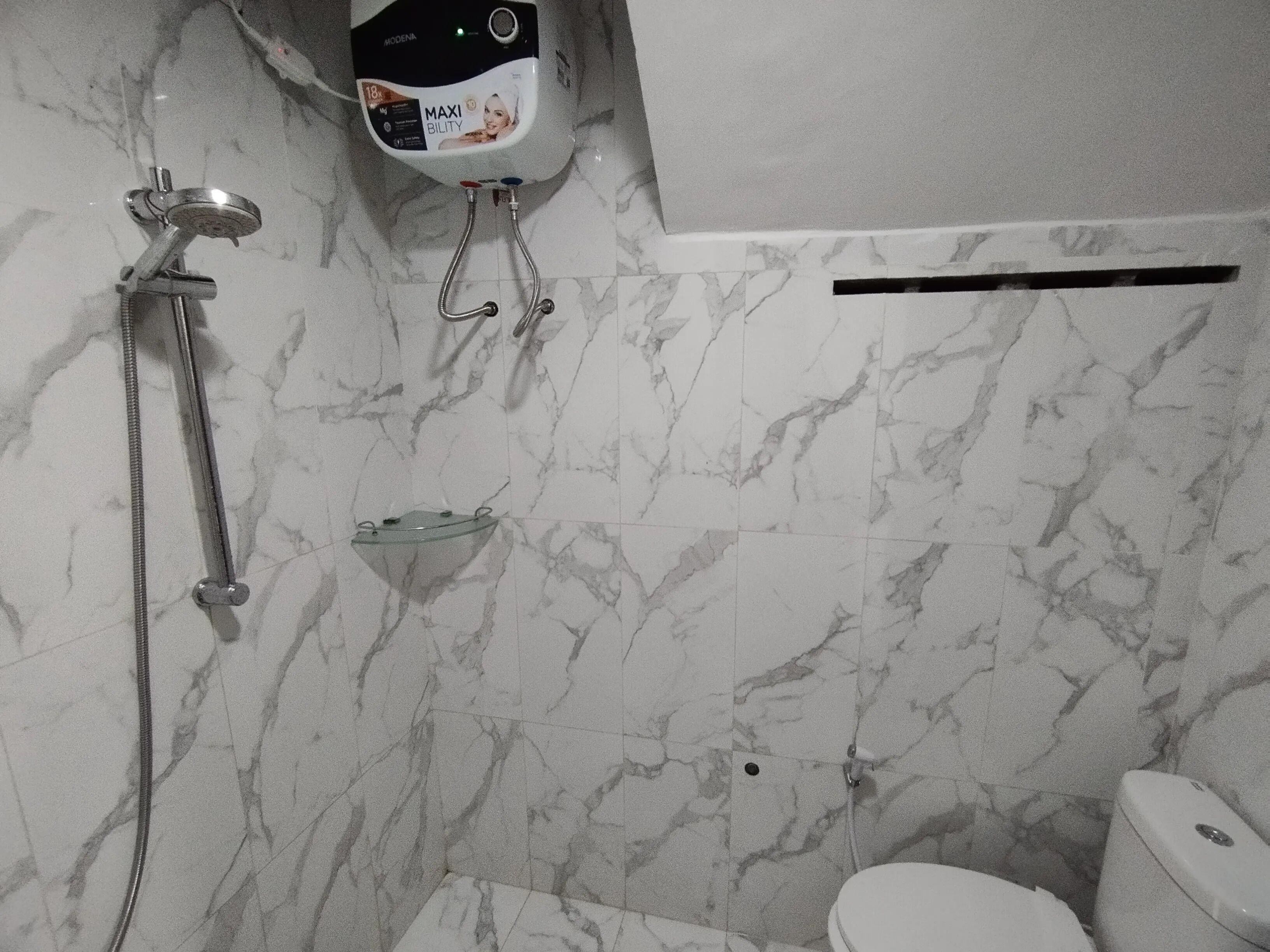 A bathroom with a shower, toilet, and a marble wall.