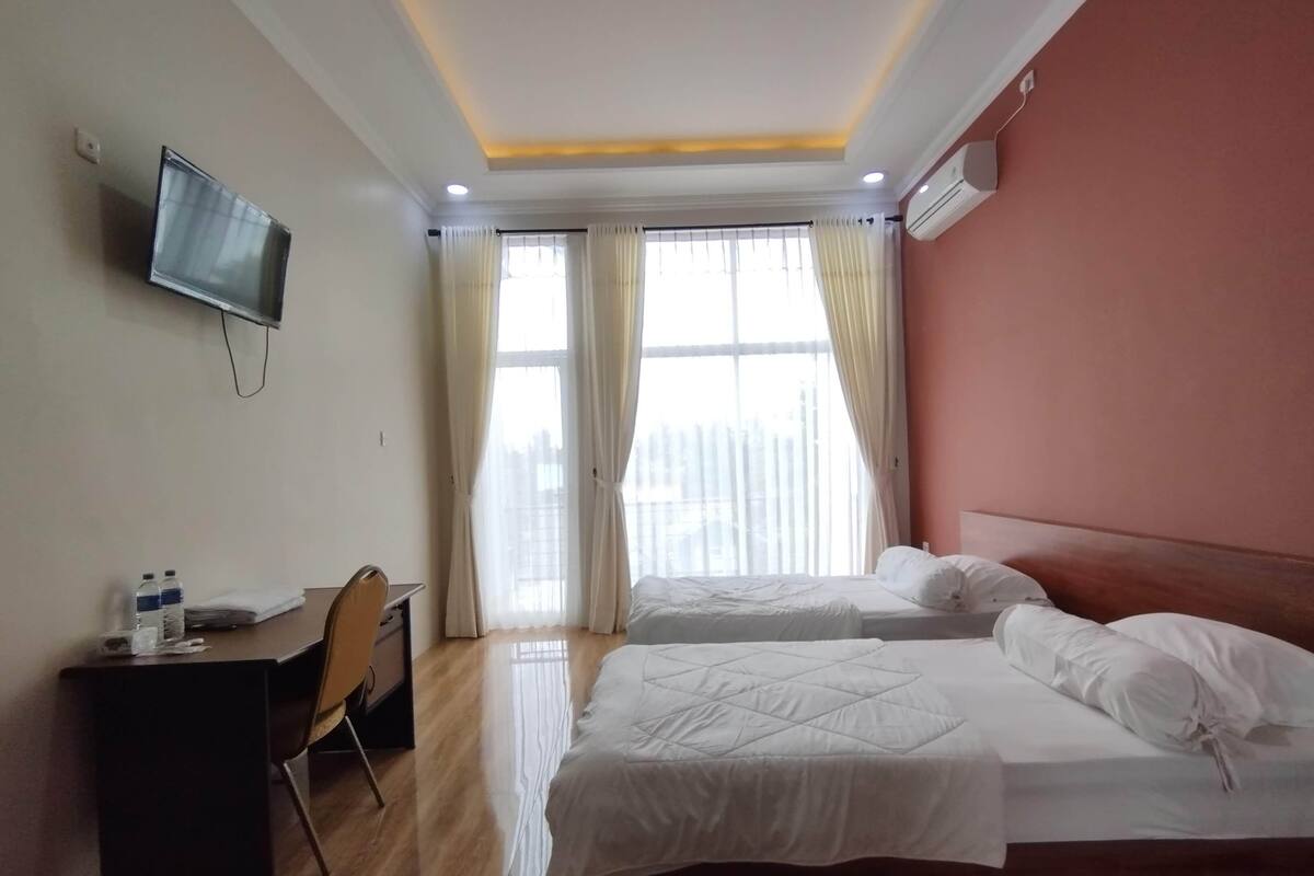 Een hotelkamer met twee bedden, een bureau, een stoel, een televisie en een raam met gordijnen.