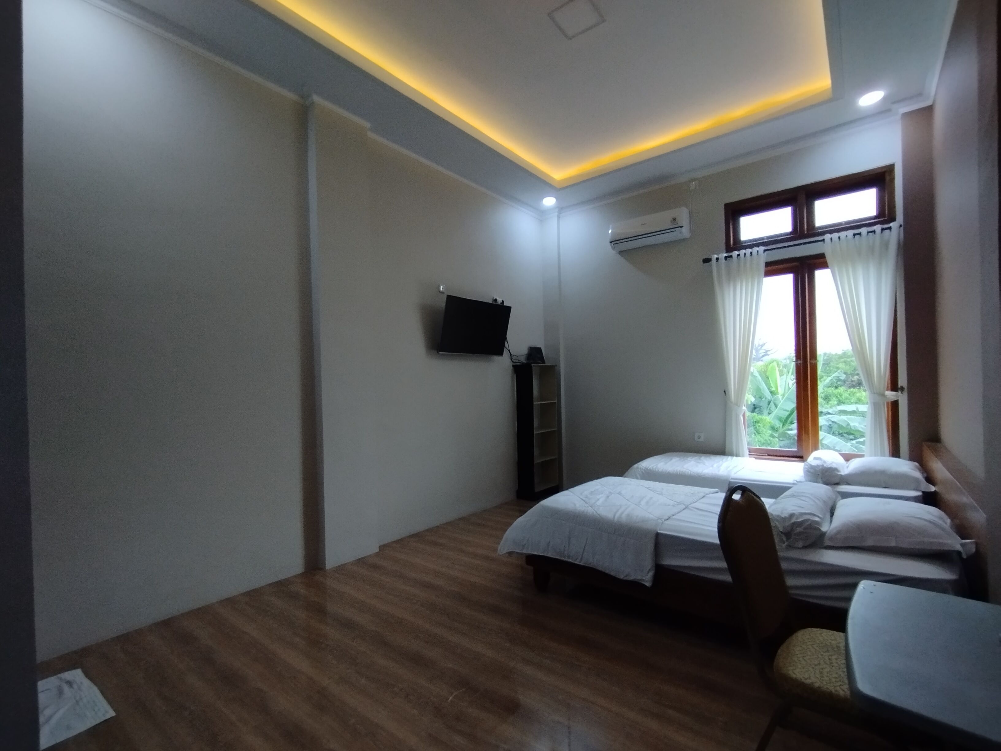 A bedroom with two beds, a desk, a chair, an air conditioning unit, and a TV mounted on the wall.