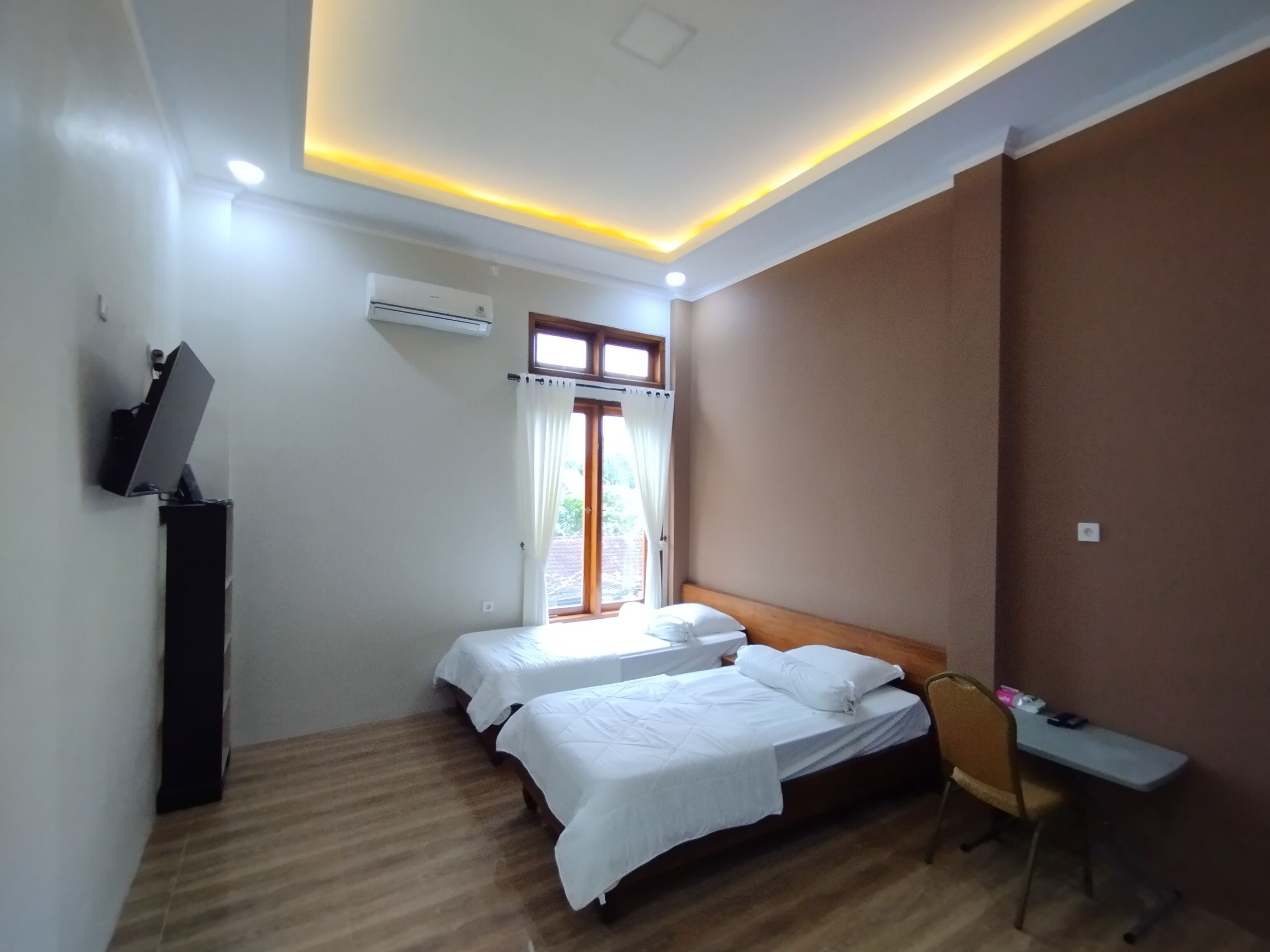 A room with two beds, a desk, a chair, and an air conditioning unit.
