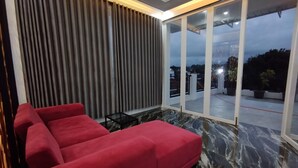 Un salon moderne avec un canapé rouge, une table basse en verre et une vue sur l’extérieur grâce à de grandes portes-fenêtres coulissantes.