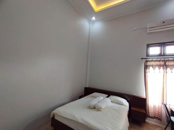 A bedroom with a bed, a window with curtains, an air conditioning unit, and a ceiling light.