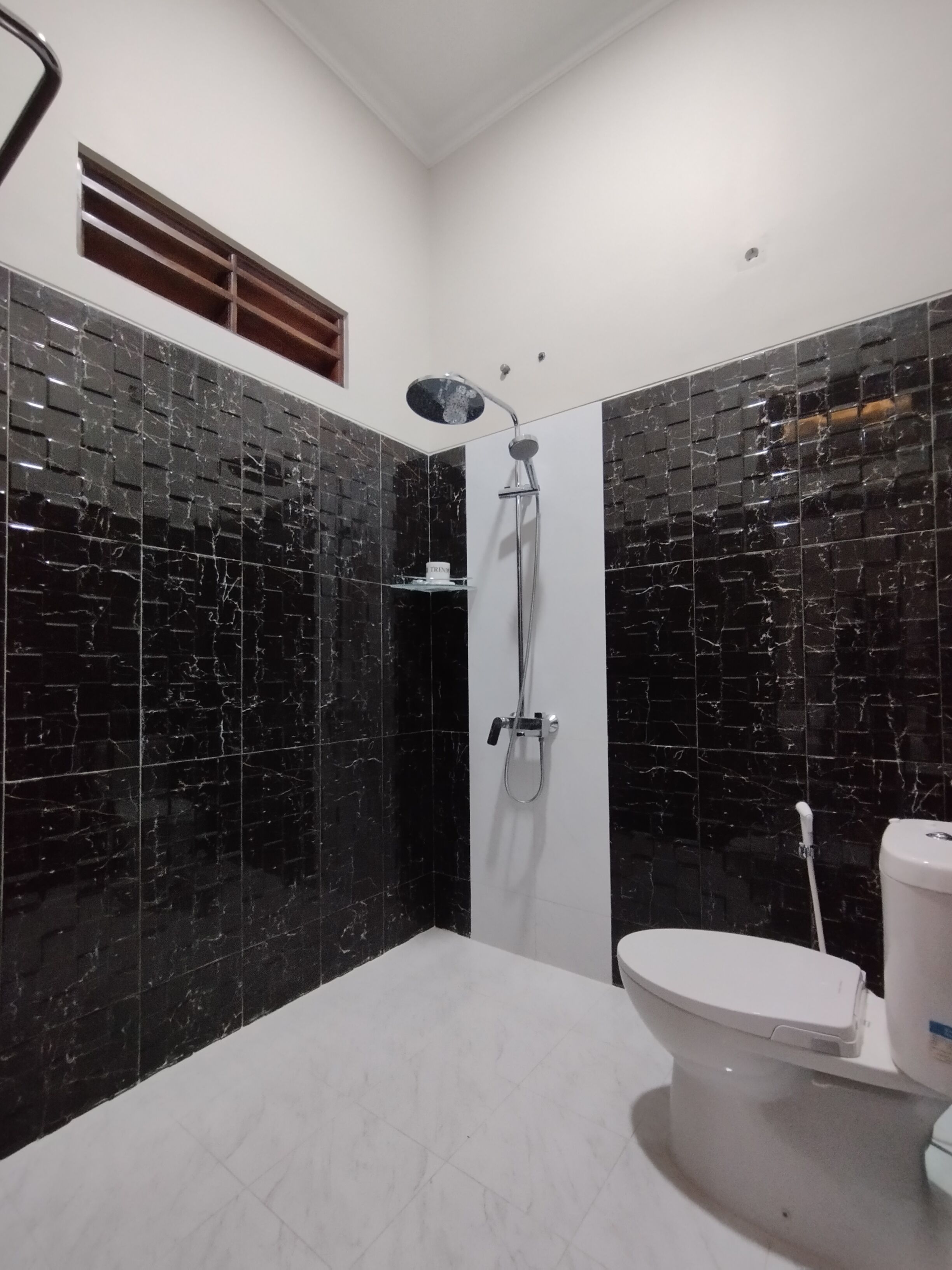 Une salle de bain moderne avec des carreaux de marbre noir, des toilettes blanches et une douche équipée d’un pommeau de douche à main.