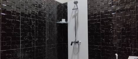 Une salle de bain moderne avec des carreaux de marbre noir, des toilettes blanches et une douche équipée d’un pommeau de douche à main.