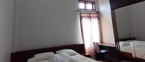A hotel room with a bed, a desk, an air conditioning unit, a window with curtains, and a ceiling light.