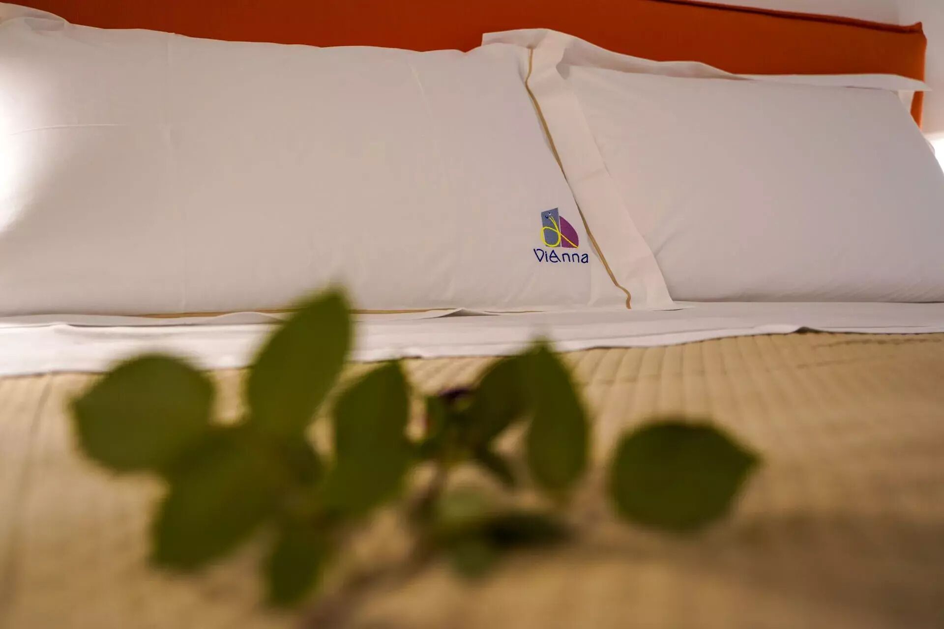 A bed with a white pillow and a small logo on it.