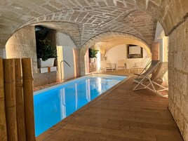 Una piscina interior con suelo de madera, arcos de piedra y sillas de descanso.