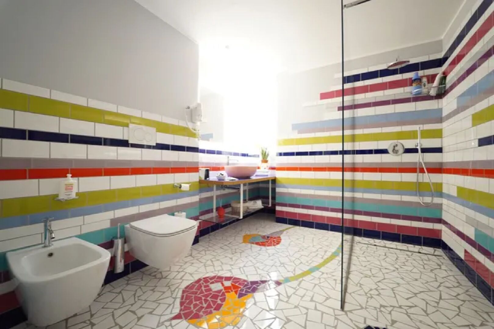 Un baño con baldosas de colores a rayas, un inodoro blanco, un bidé y una zona de ducha.