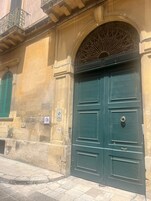 Un edificio histórico con una puerta verde doble de gran tamaño, fachada de piedra y un balcón de metal con barandillas elaboradas.