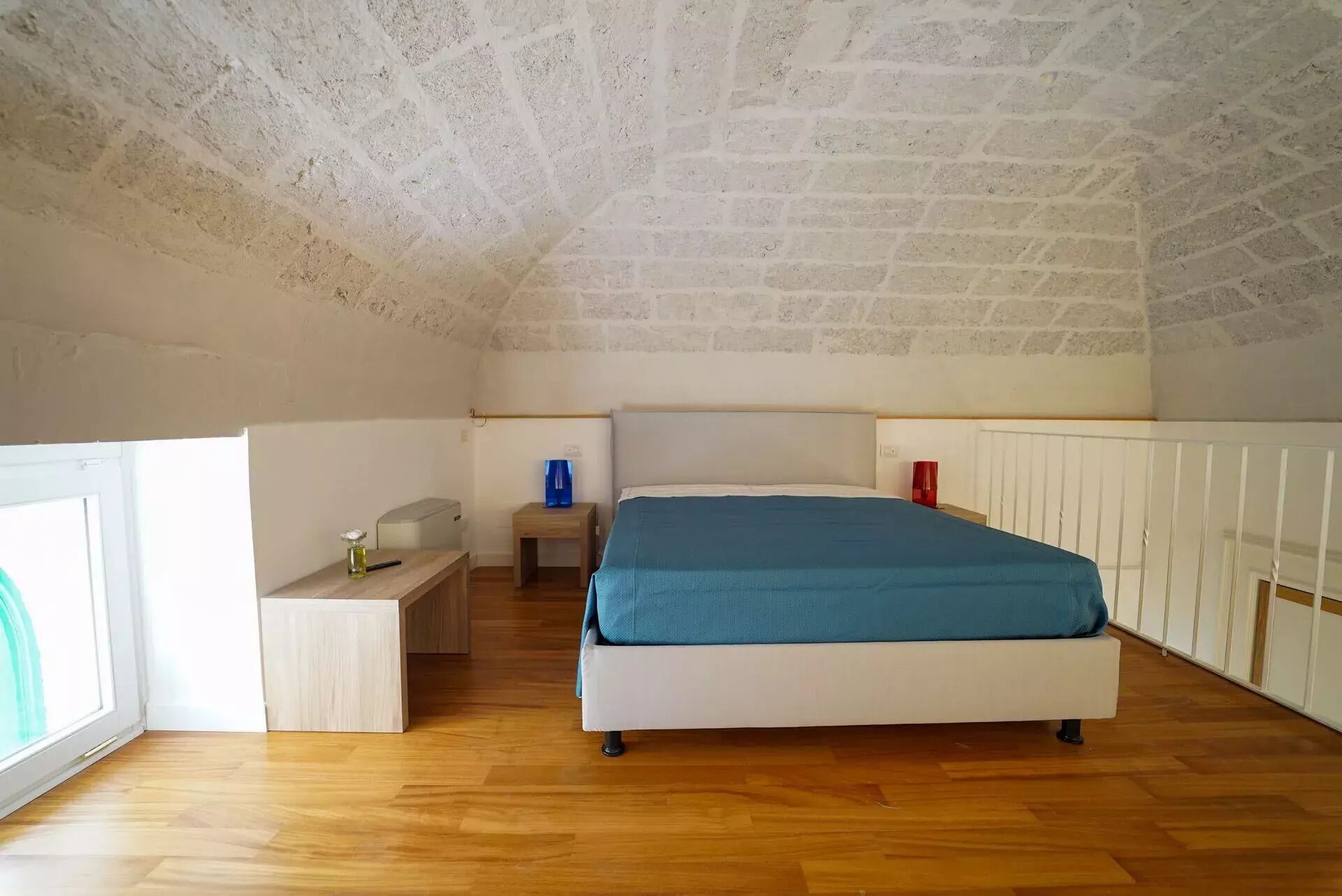 Une chambre avec un plafond en pente, un lit, une table de chevet, une petite table et une fenêtre.