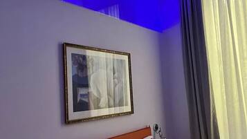 Une chambre d’hôtel avec un lit, un tableau encadré au mur et une fenêtre avec des rideaux.