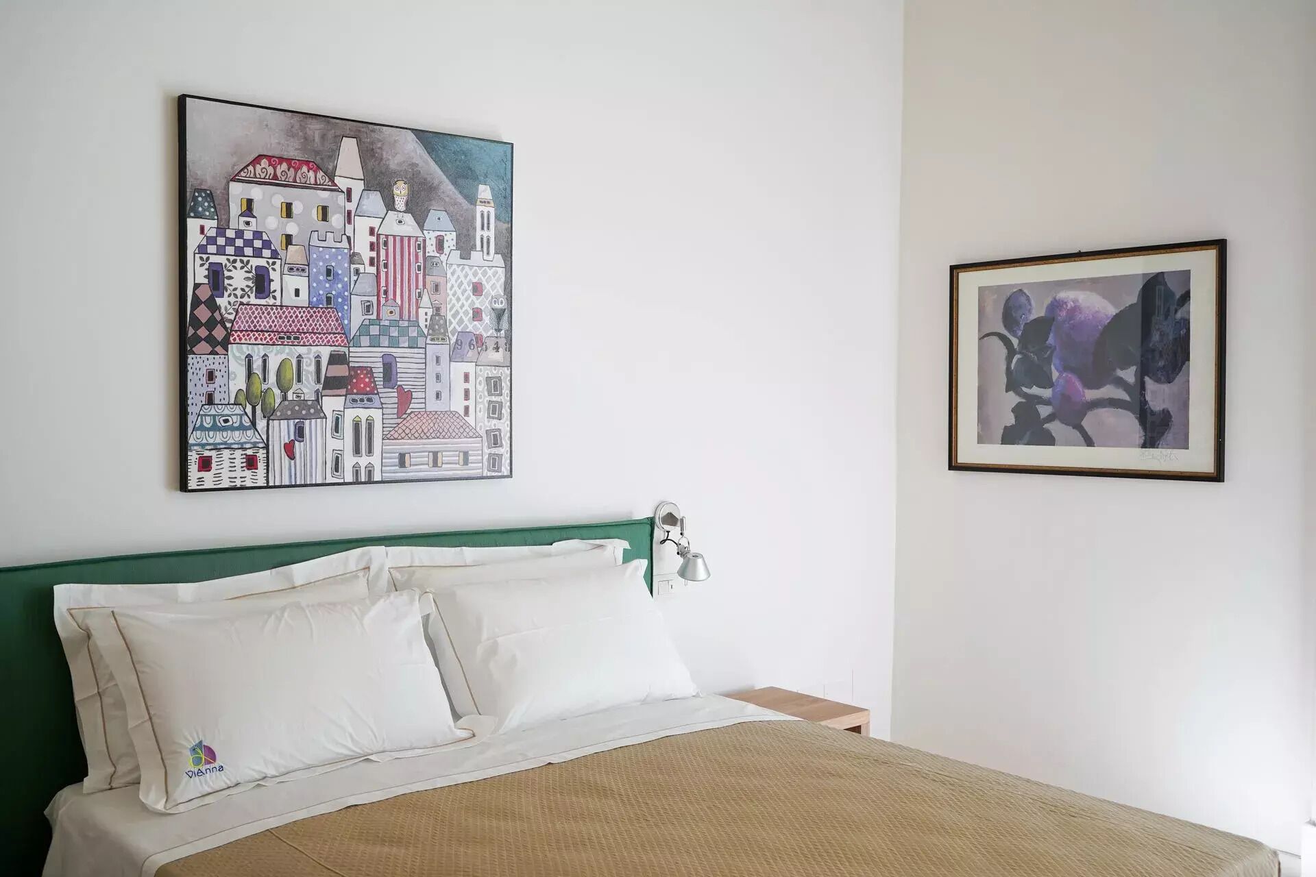 Een slaapkamer met een bed, kussens en twee kunstwerken in een lijst aan de muur.