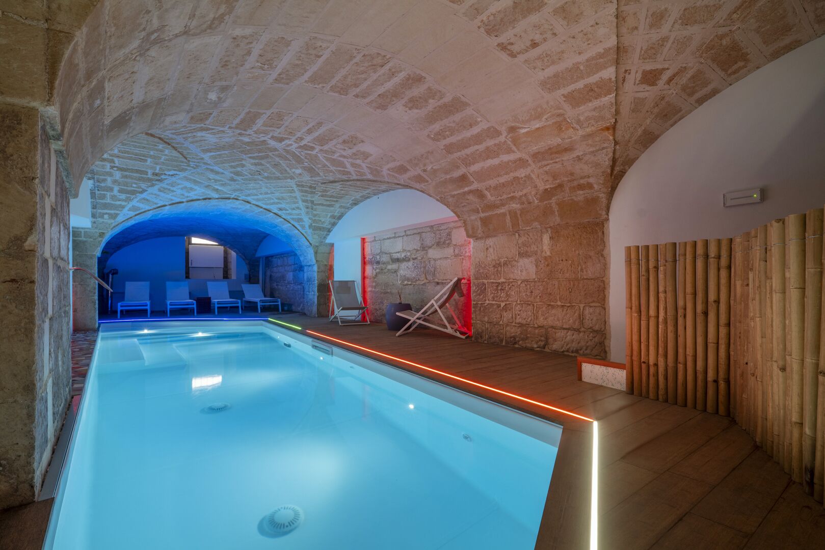 Piscina de diseño moderno rodeada de muros de piedra y elementos de madera, con una vista despejada del área de la piscina y sus asientos.